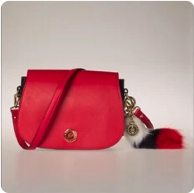 Red leather handbag with gold hardware and a black, white, and red fur charm, shown before background removal.