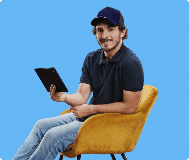 Seated man holding a tablet on a clean blue background after portrait background replacement and retouching.