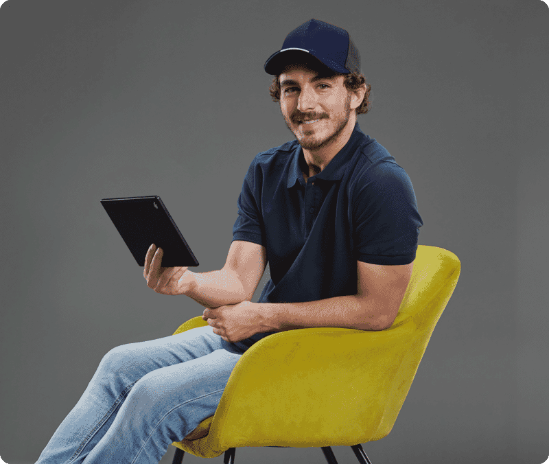 Original portrait of a seated man holding a tablet on a gray studio background before background editing.