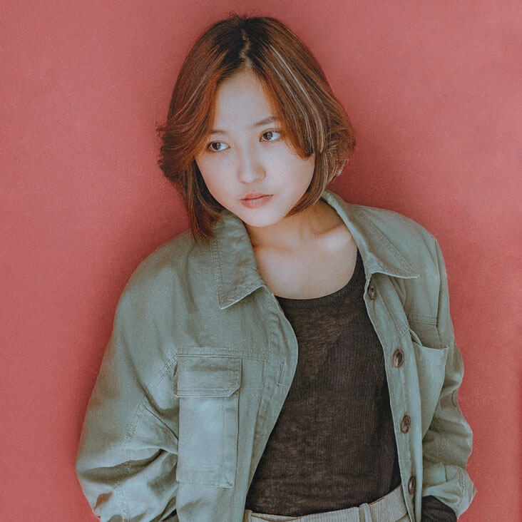 Portrait of a woman wearing an olive jacket and brown top against a red backdrop, after expert photo retouching.