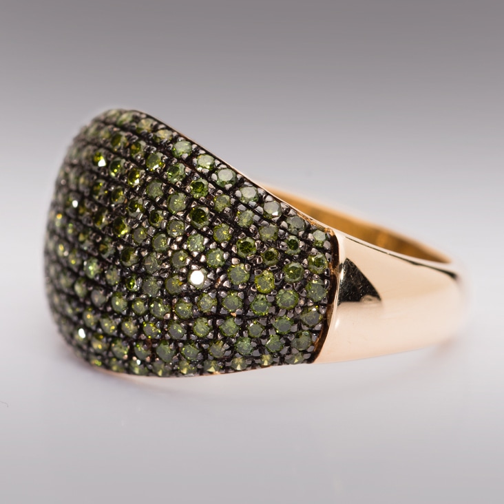 Gold ring featuring green gemstones, shown with visible camera reflections on its surface before editing.