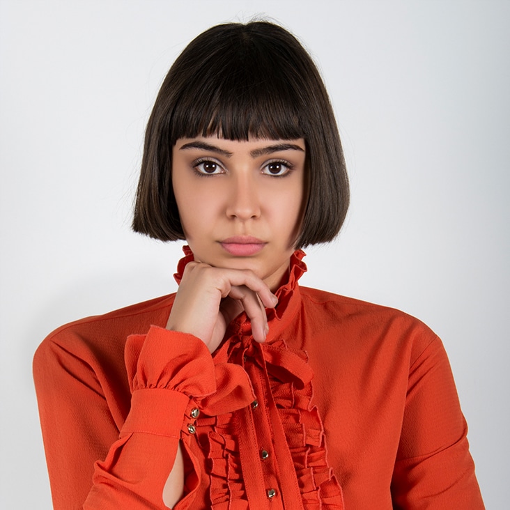 Woman in orange blouse with smooth, airbrushed skin and defined features, showcasing advanced portrait retouching.