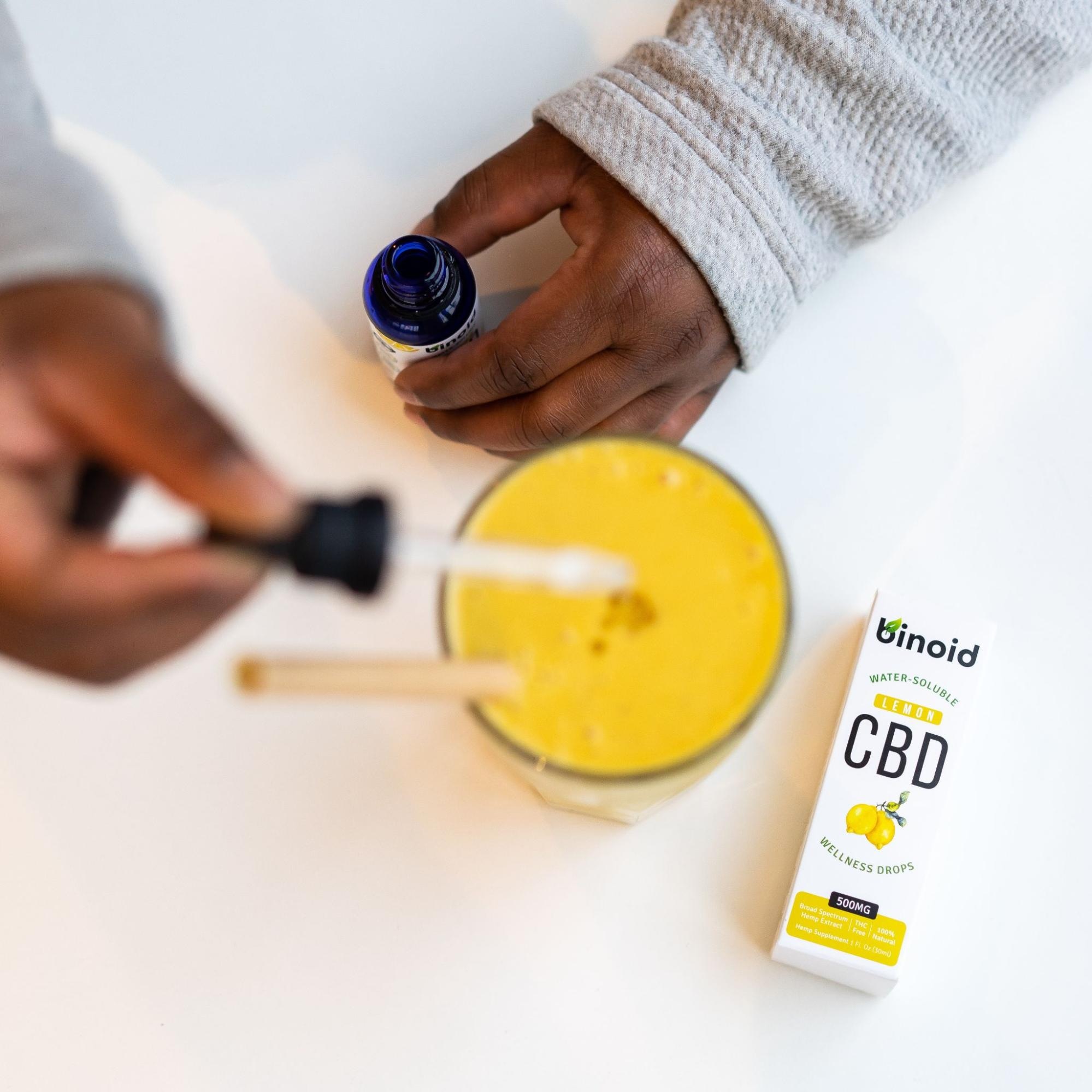 CBD wellness drops bottle with a pipette held over a yellow beverage, illustrating product use.