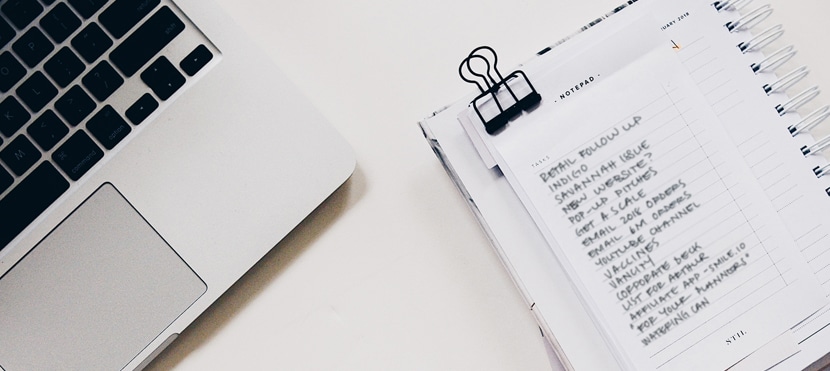 Top view of a laptop and organized notepad with a to-do list on a clean workspace.