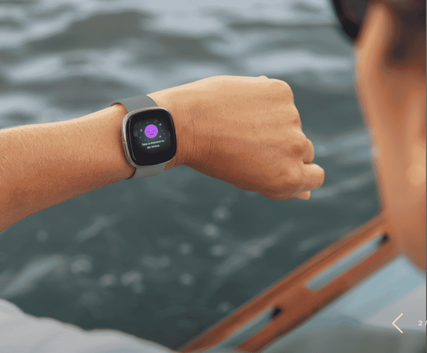 Person wearing Fitbit smartwatch by water, screen displaying relaxation reminder