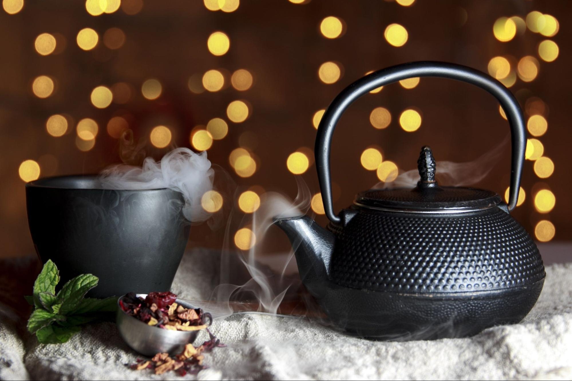 Black teapot and steaming cup with dry ice effect, warm bokeh lights in background