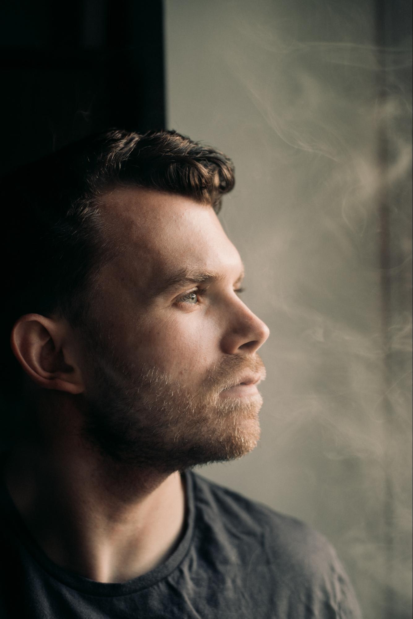 Profile of man looking out window, illuminated by soft natural light with subtle background smoke effect