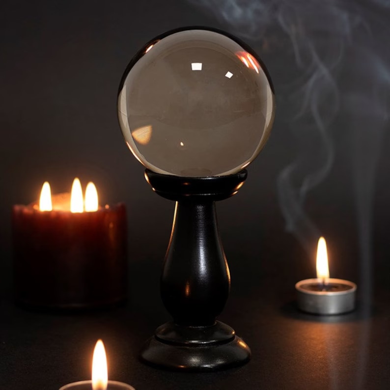 Crystal ball on black stand with candles and smoke in a dark, mystical setting