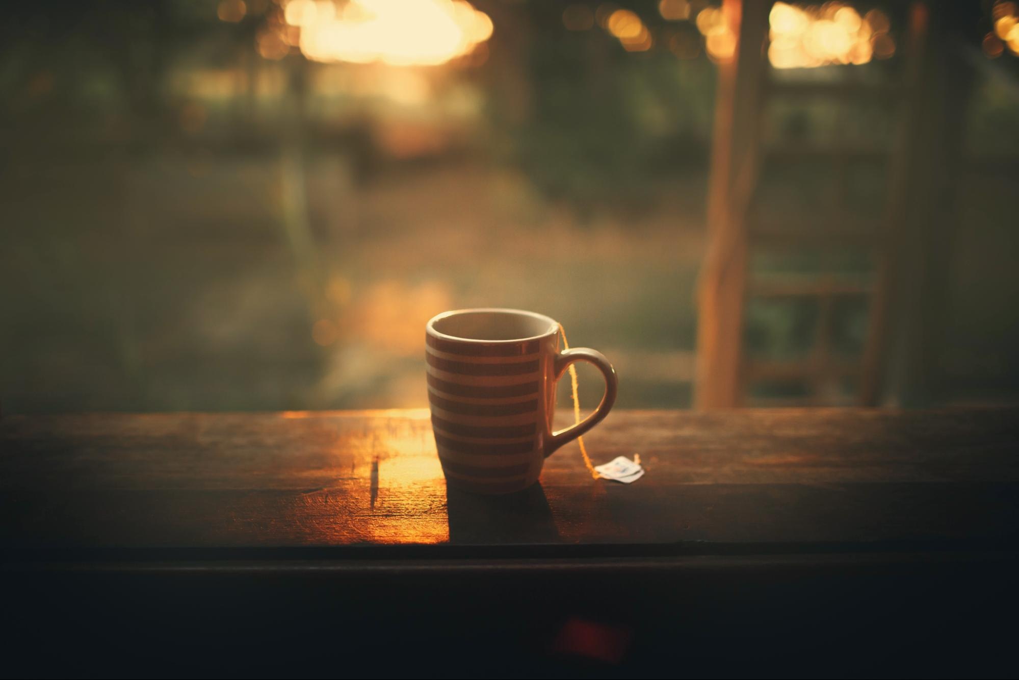 Striped tea cup with tea bag on a wooden table, illuminated by warm morning light at sunrise