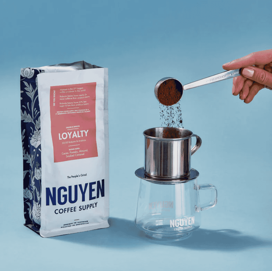 Nguyen Coffee Supply Loyalty blend next to a phin filter setup with coffee grounds being poured in.
