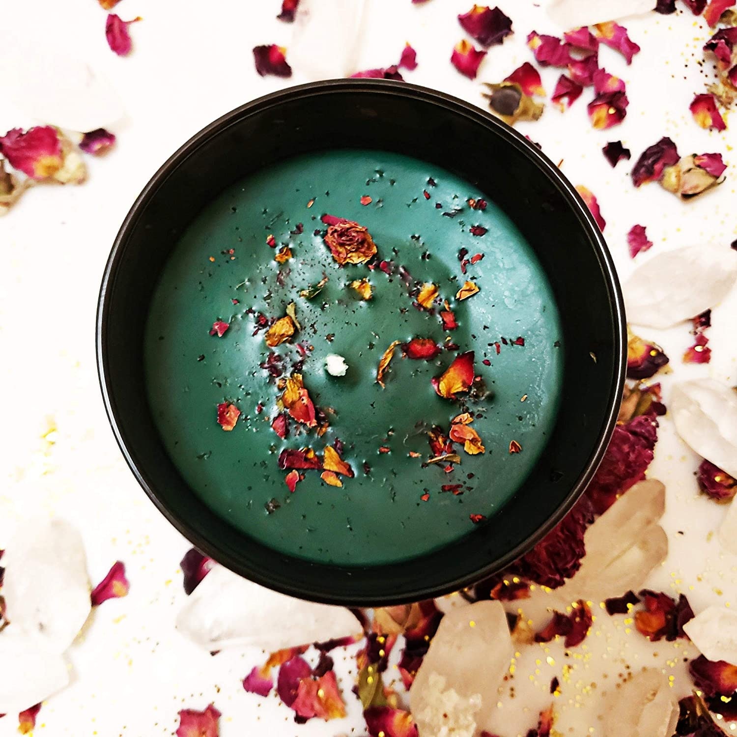 Top view of a green candle with dried floral accents, surrounded by rose petals and crystals.