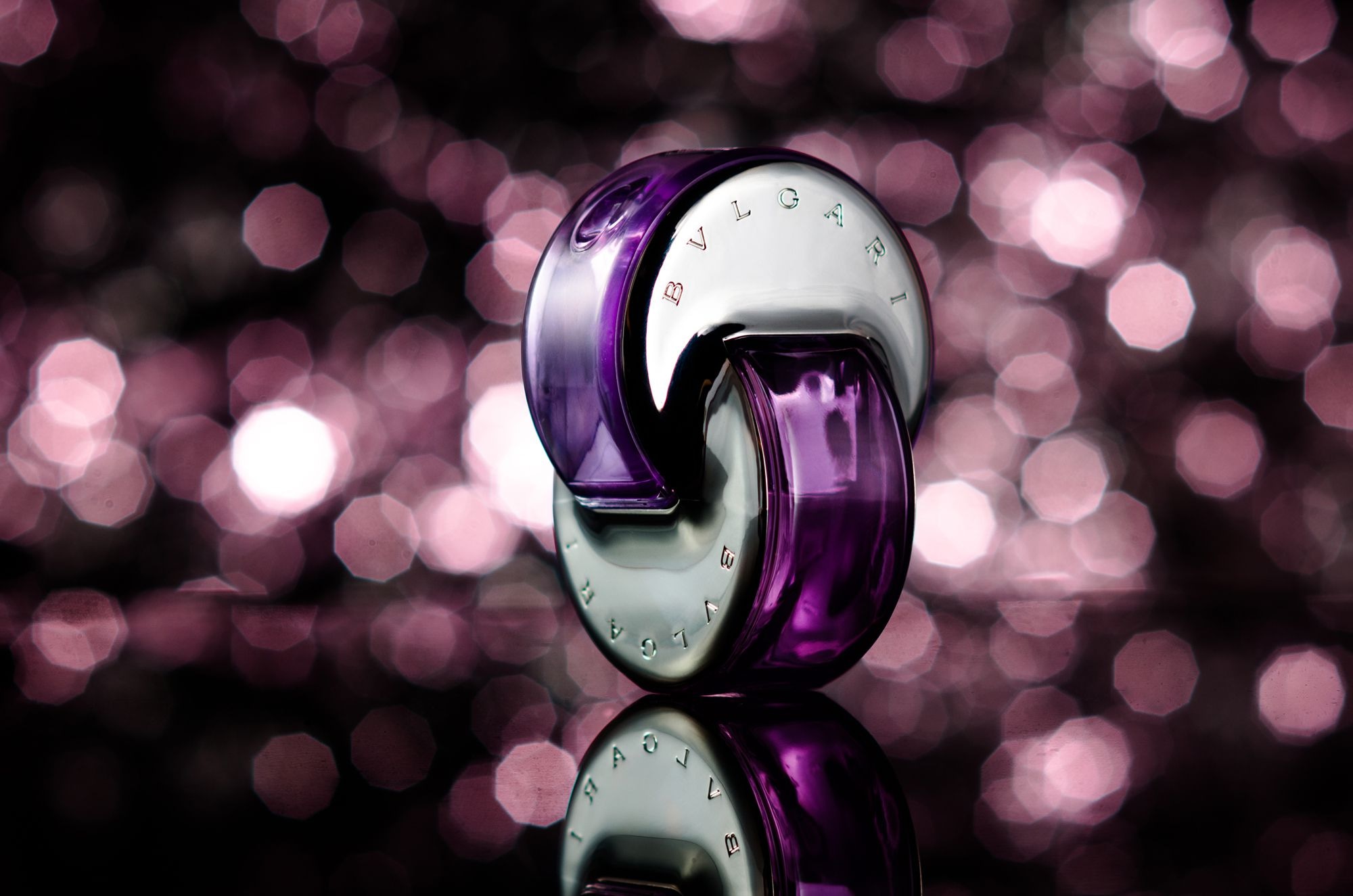 BVLGARI perfume bottle with purple accents on reflective surface, set against a soft bokeh background.