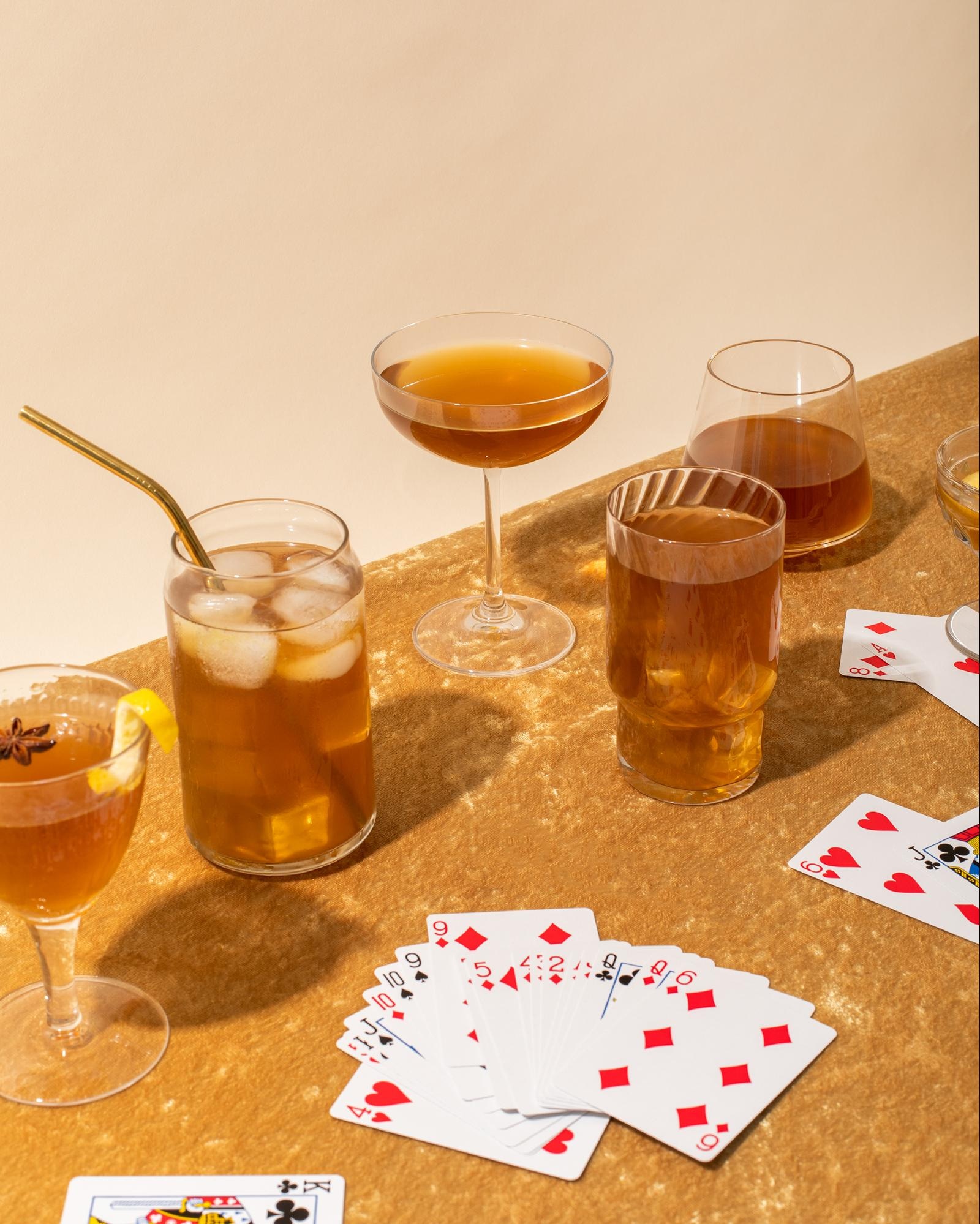 Assorted cocktails on a gold table with playing cards, creating a stylish game night setting.
