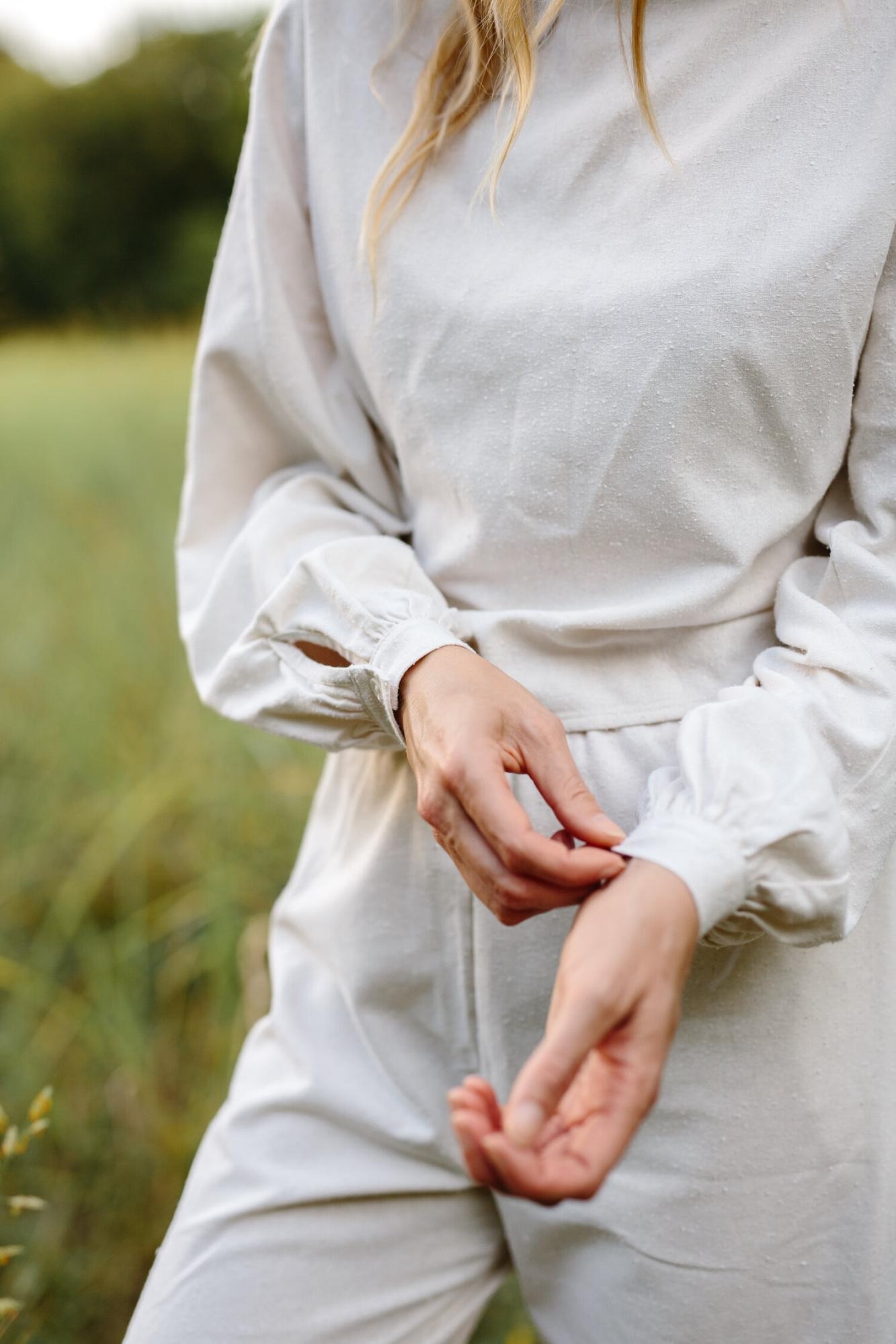 Close-up of hands adjusting sleeve on light-colored outfit, captured outdoors with natural lighting.