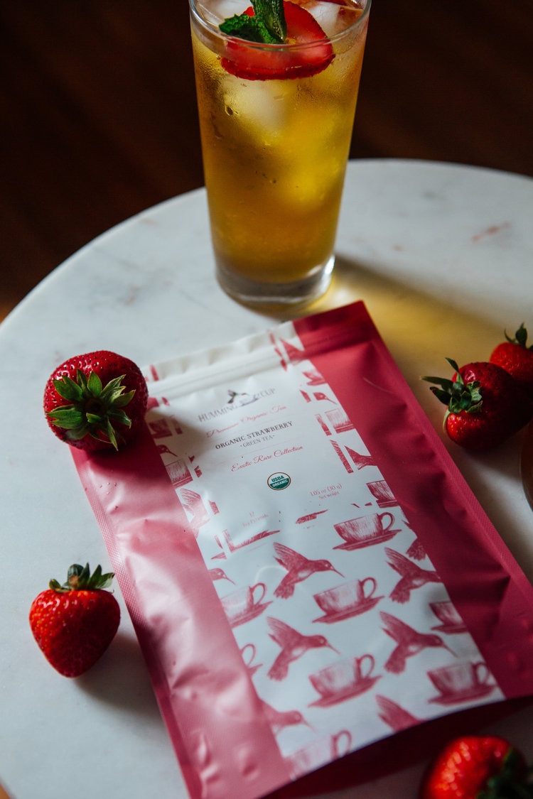 Organic strawberry iced tea with fresh strawberries and tea packaging on marble table.