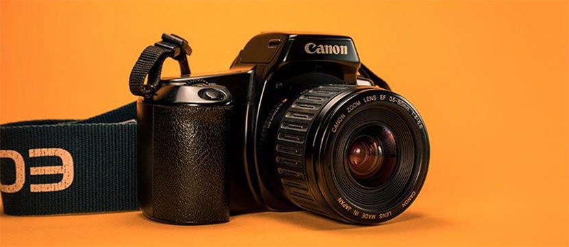 Canon DSLR camera with lens cap on, placed against an orange background.