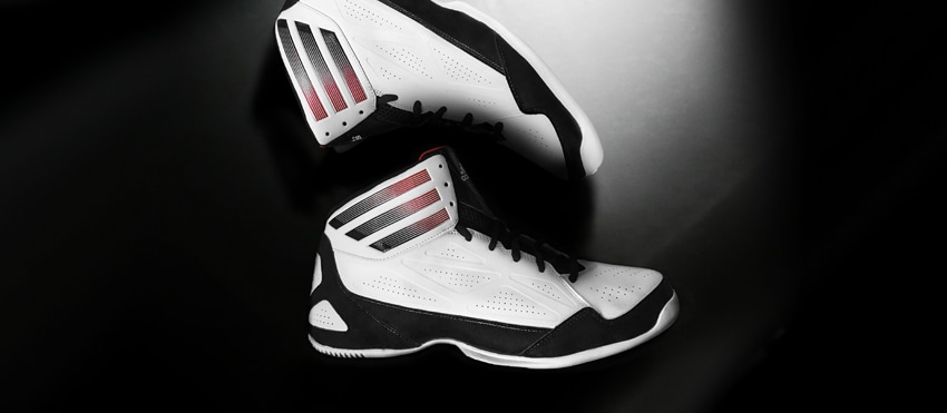 Pair of black and white athletic shoes with red accents on a dark background.
