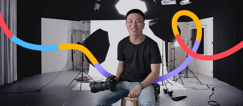 Photographer seated in a professional studio with lighting and camera equipment, colorful graphic elements in the foreground.