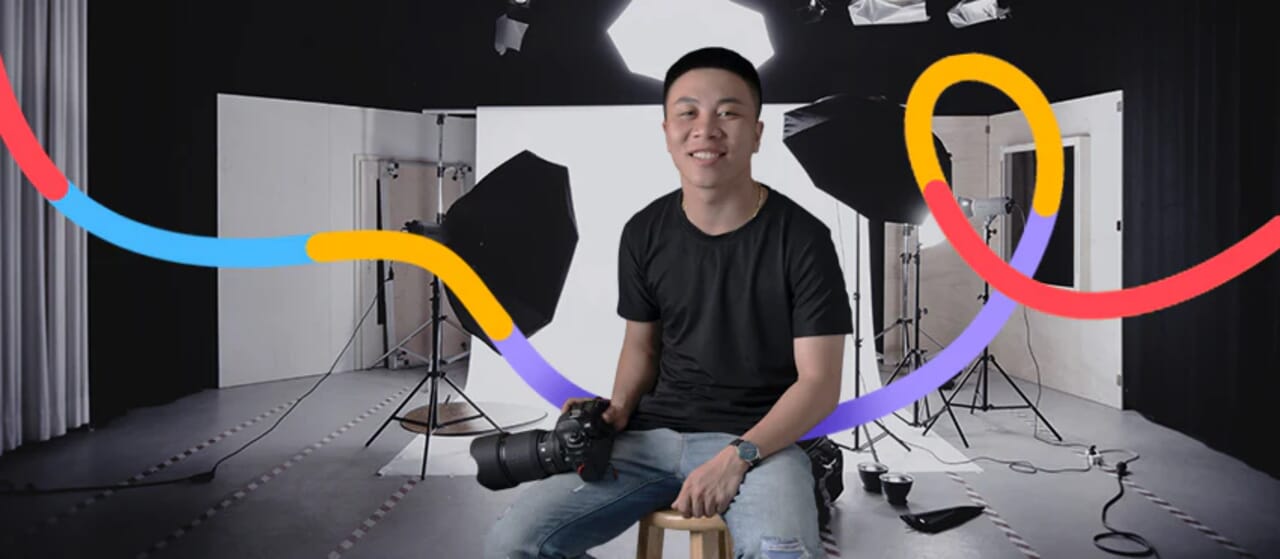 Photographer seated in a professional studio with lighting and camera equipment, colorful graphic elements in the foreground.