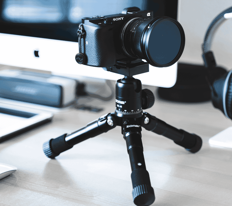 Sony camera mounted on a mini tripod in a desktop workspace with computer background.
