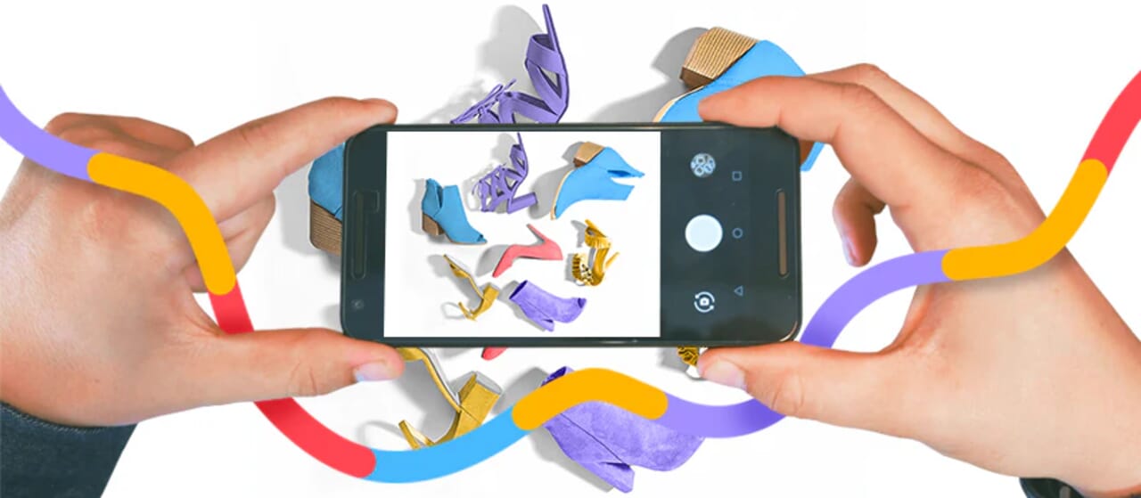 Hands holding a smartphone photographing a colorful collection of shoes, with a vibrant ribbon design in the background.