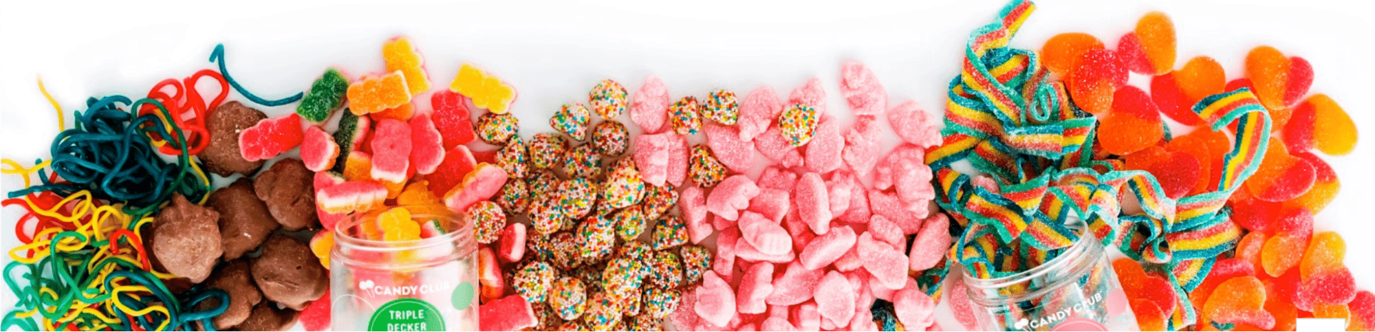 Colorful assortment of gummy candy including rainbow strips, chocolate clusters, sour hearts, and sprinkles, spilling out of open Candy Club jars.