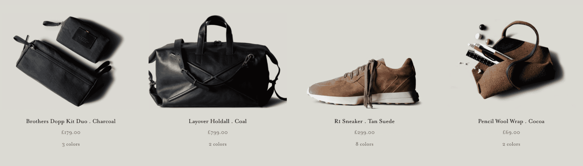 Premium men’s accessories including a charcoal dopp kit set, black leather holdall, tan suede sneakers, and a cocoa wool pencil wrap.