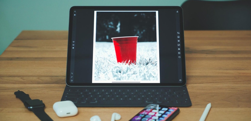 Tablet displaying a red cup in color against a black and white background, surrounded by tech accessories on a desk