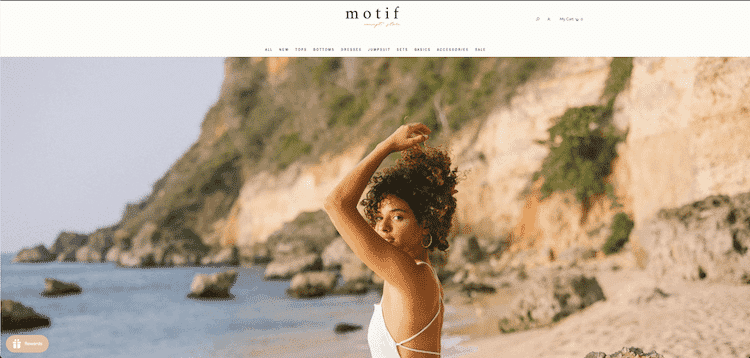 Model posing on a rocky beach in a white outfit for Motif Concept Store's fashion banner with scenic coastal background.