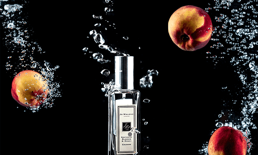 Perfume bottle with peaches and water splash, emphasizing dynamic product presentation for ecommerce.