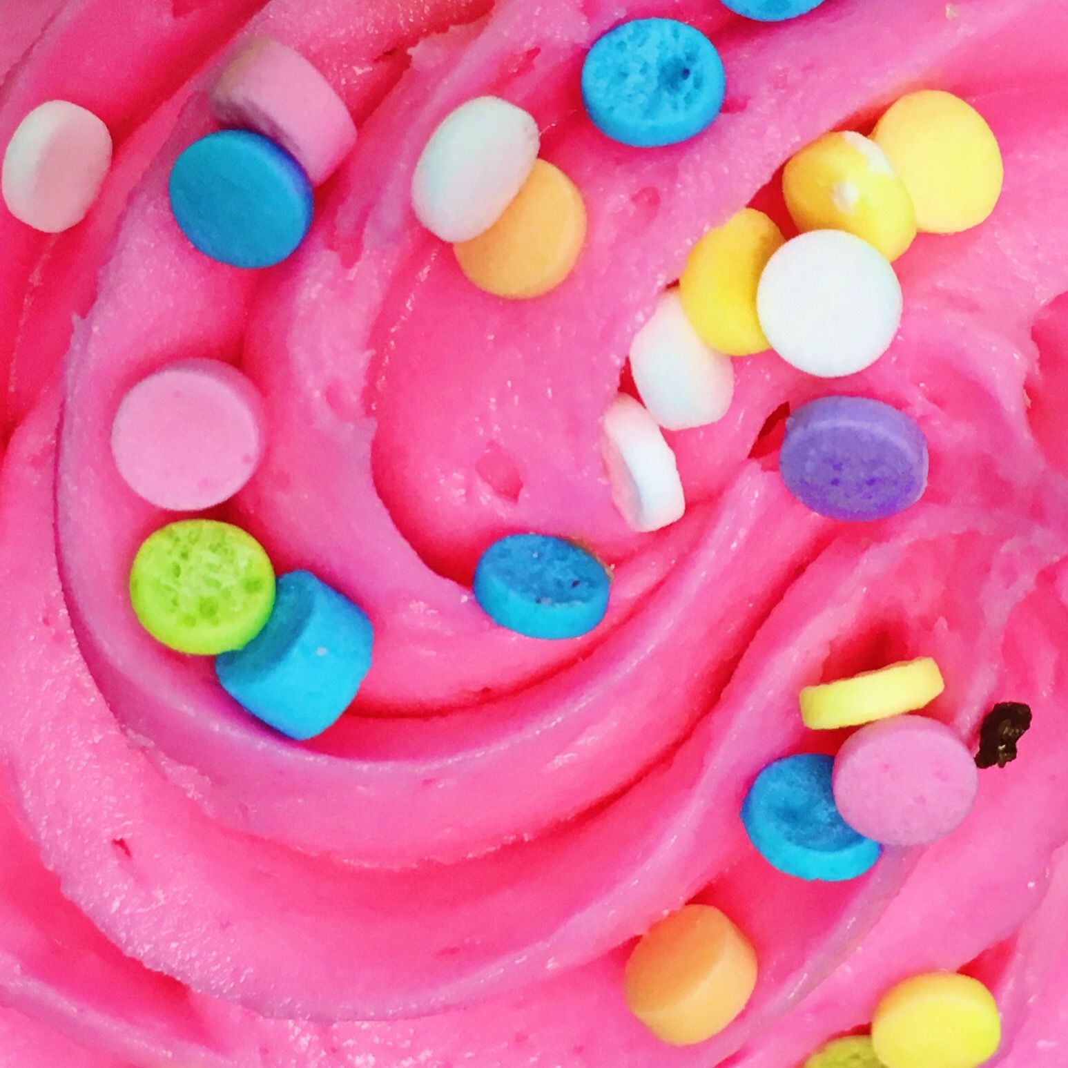 Close-up of vibrant pink frosting swirled with colorful round sprinkles