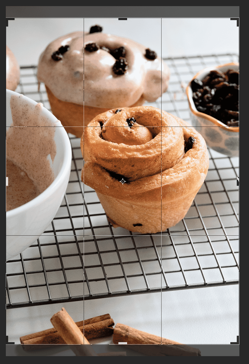 Cinnamon rolls and frosted buns on a cooling rack with cropping guides for photo editing