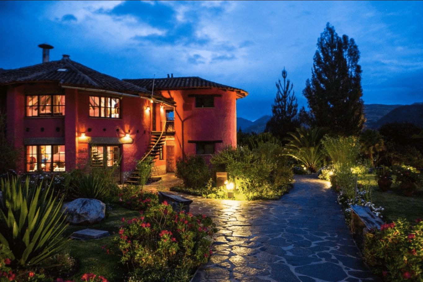 Pink country house with outdoor lights illuminating garden pathway at dusk.