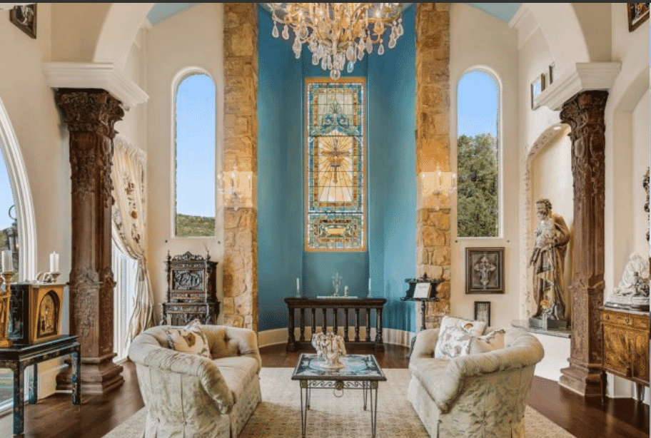 Luxurious living room with stained glass window, chandeliers, and antique furnishings.