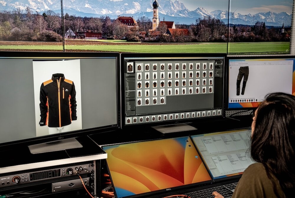 Photographer editing high-volume apparel images on multiple monitors, showcasing a jacket and pants.