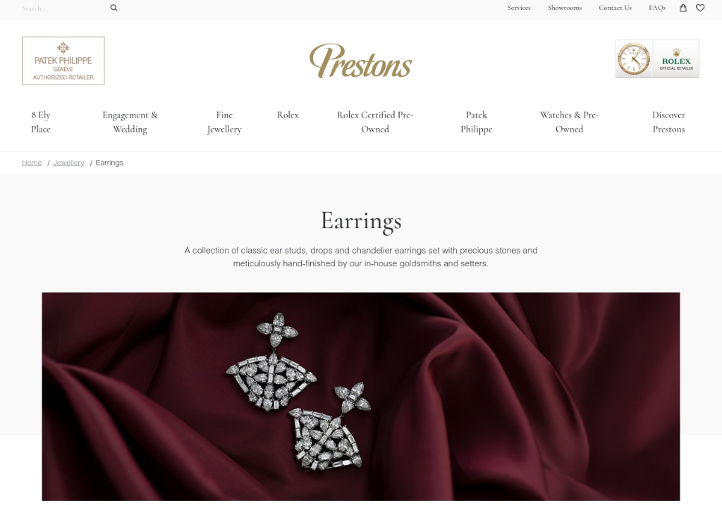 Prestons fine earrings collection featuring diamond-studded chandelier earrings on a burgundy fabric background