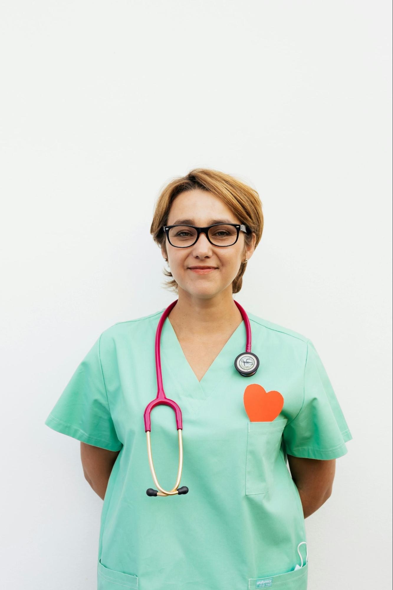 Female healthcare professional in scrubs with stethoscope against plain background