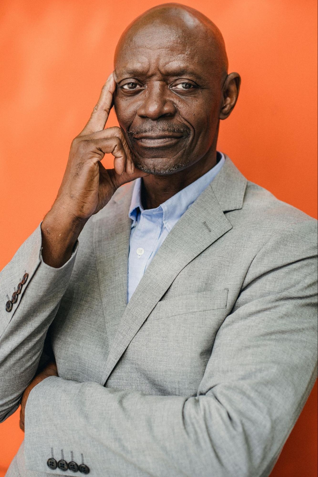 Confident man in gray suit with thoughtful expression, posed against orange background