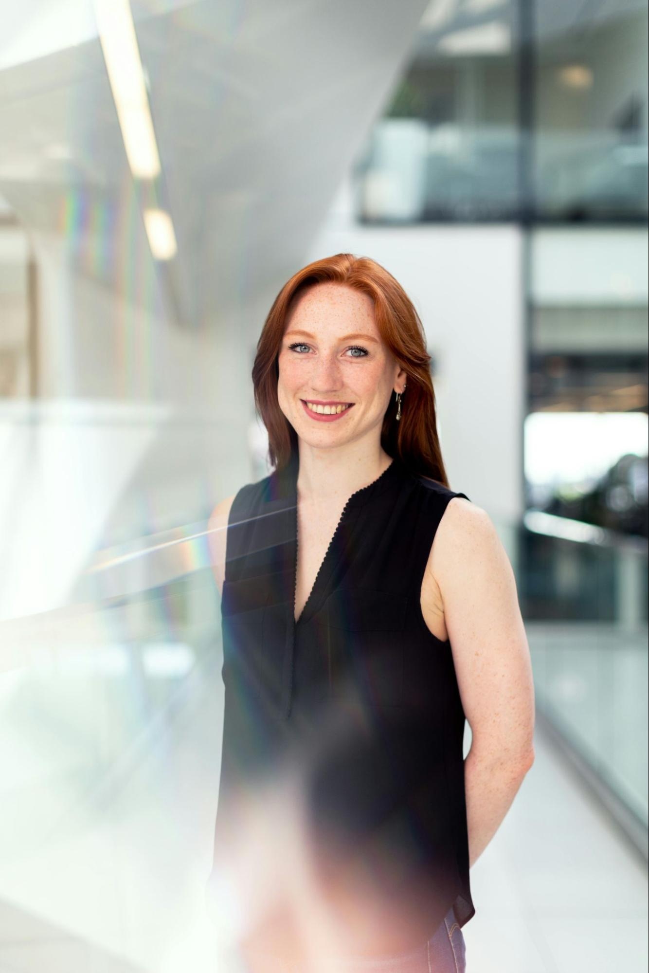 Smiling woman in sleeveless top standing in a bright, modern office with natural light reflections
