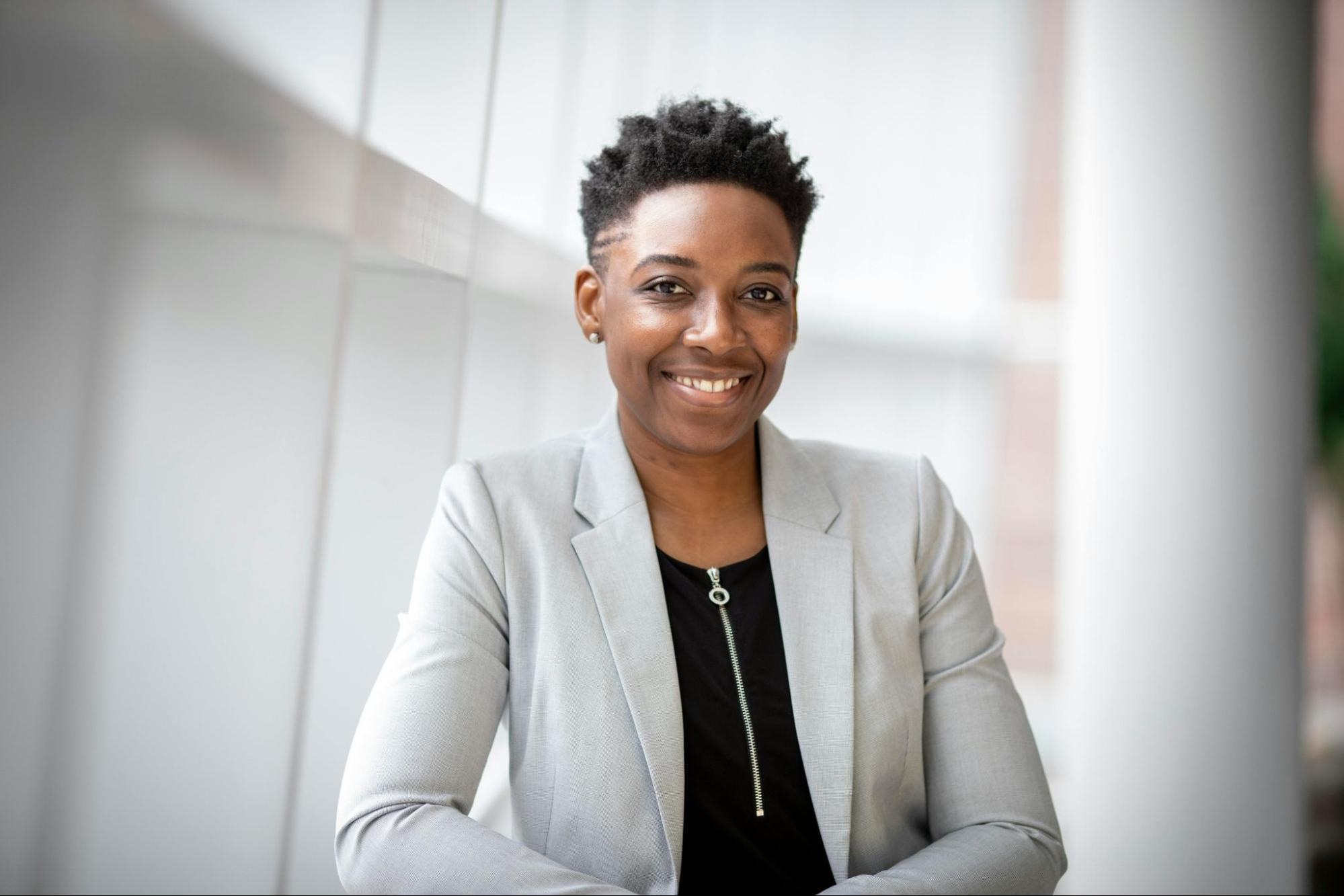 Confident woman in gray blazer smiling in bright, modern office environment