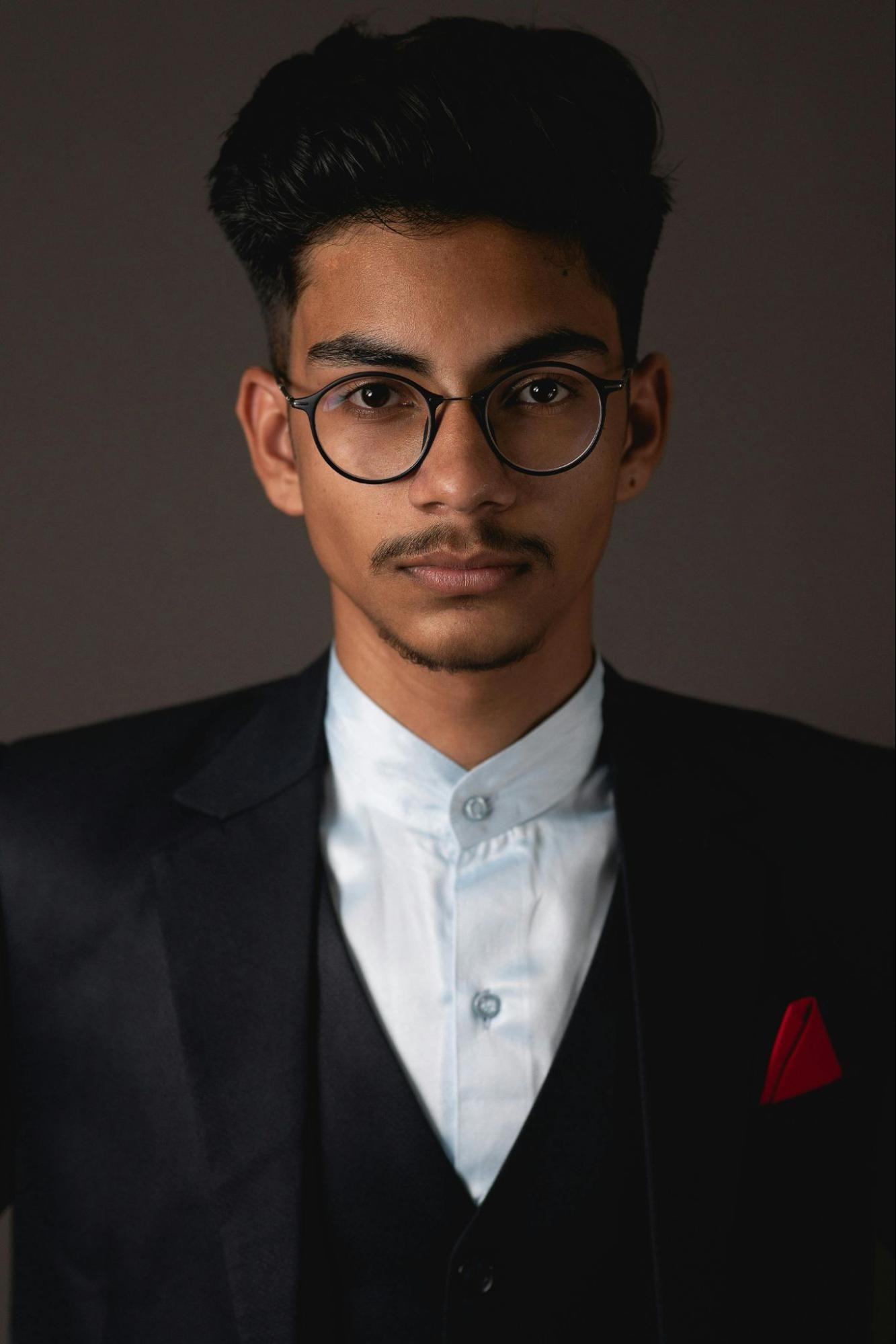 Young man in glasses and suit with red pocket square against a dark background
