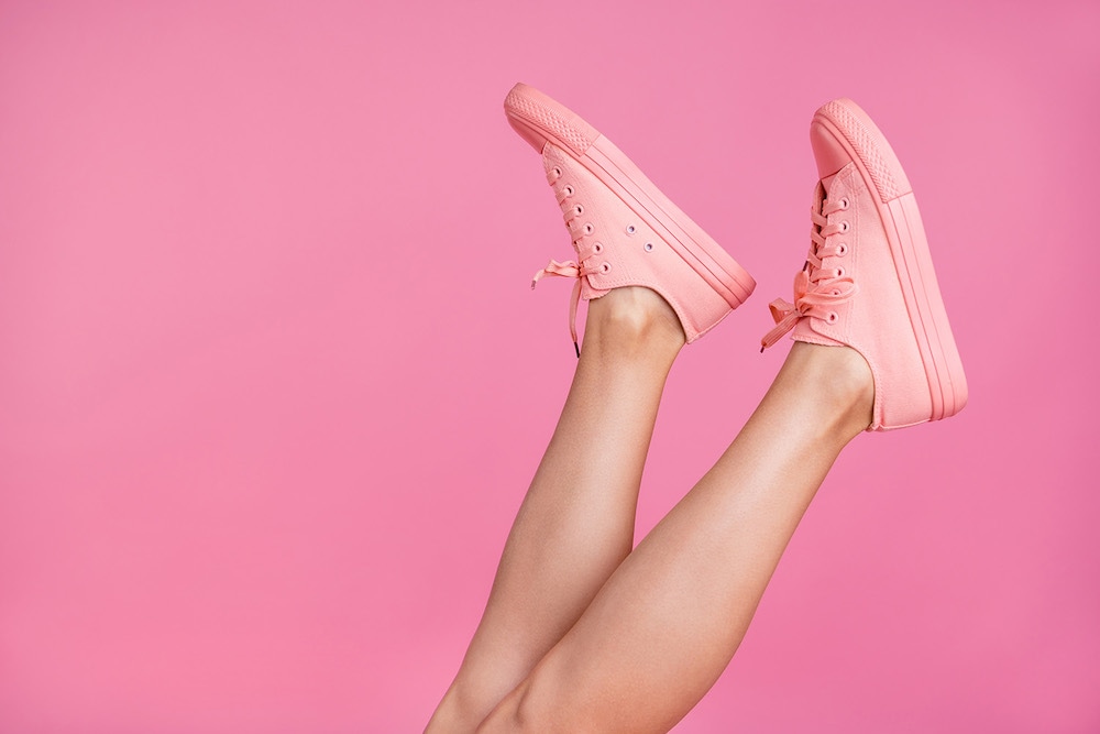 Legs in pink sneakers raised against a pink background, ideal for background editing tutorials.