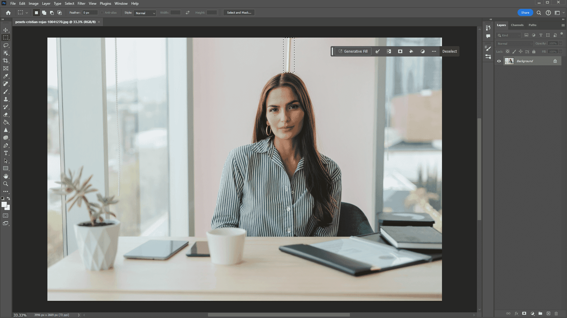 Image in Photoshop showing a woman in an office with selected background area using Generative Fill tool to remove distractions.
