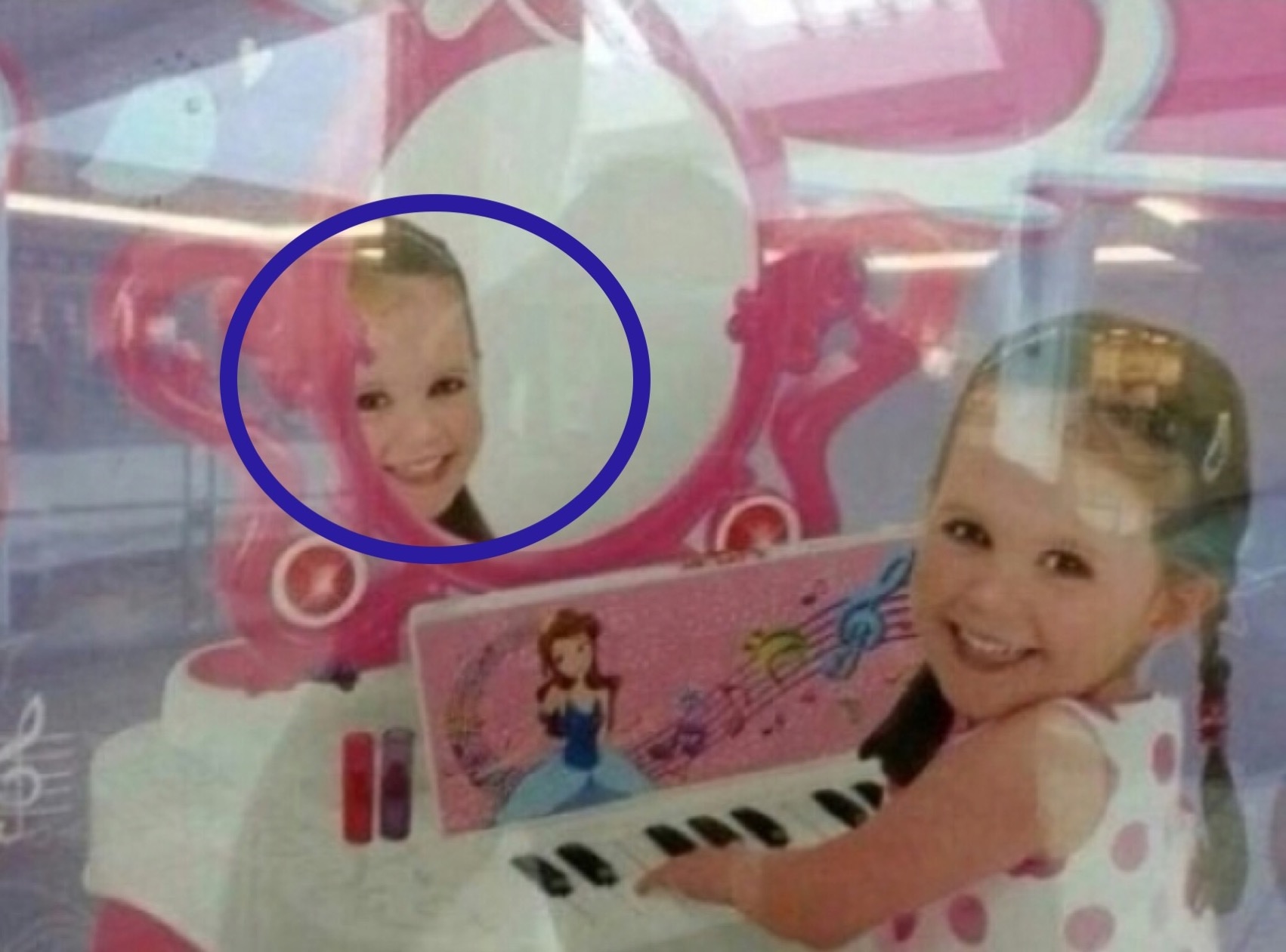 Young girl playing at pink toy piano with her reflection in a toy mirror.