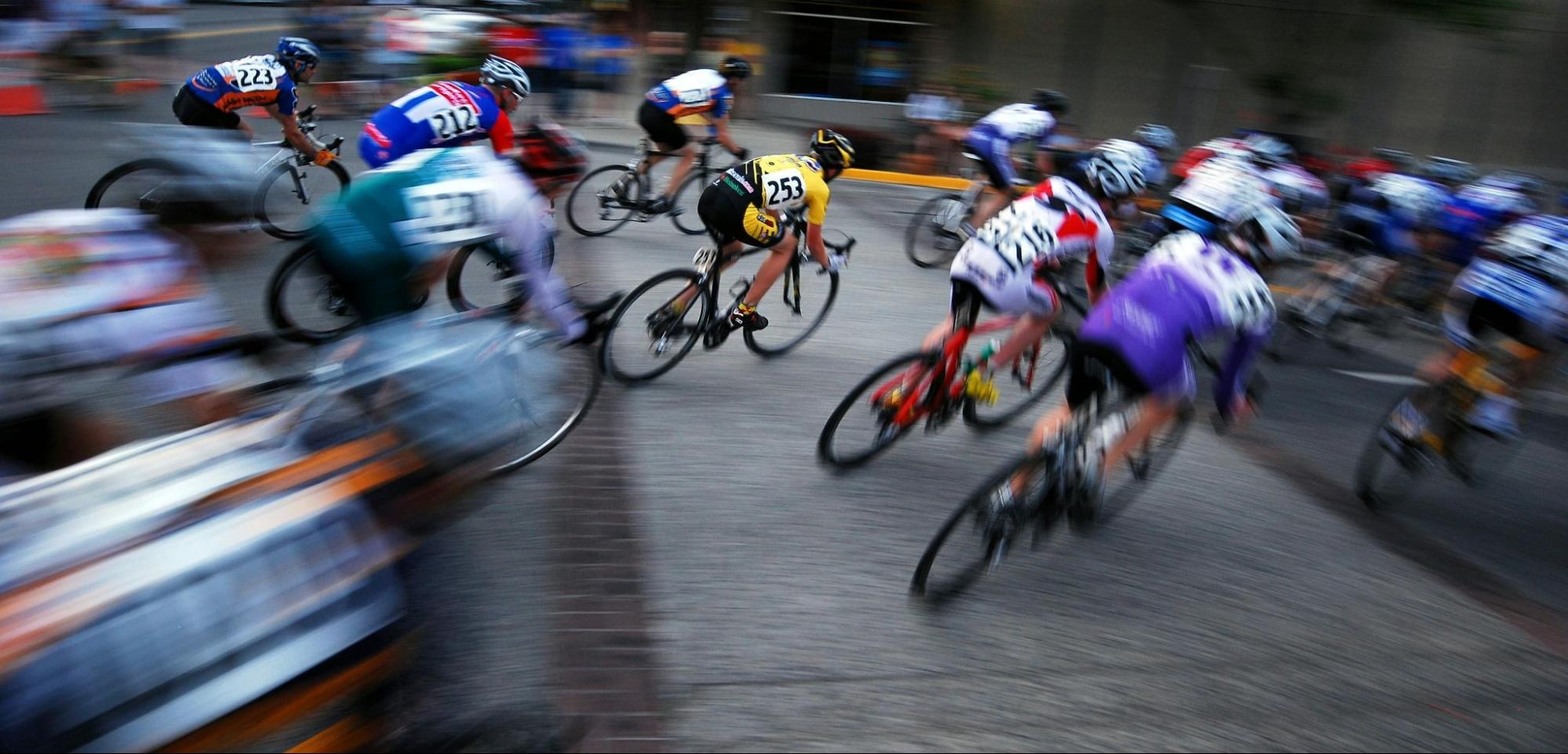 High-speed group cycling race with motion blur emphasizing dynamic movement and competition intensity on city streets.