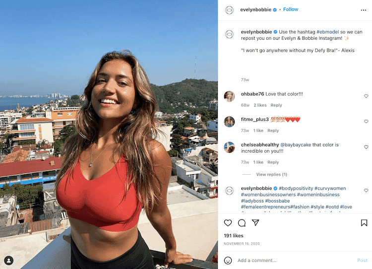 Customer wearing Evelyn & Bobbie Defy Bra in red, smiling on a rooftop with a scenic view