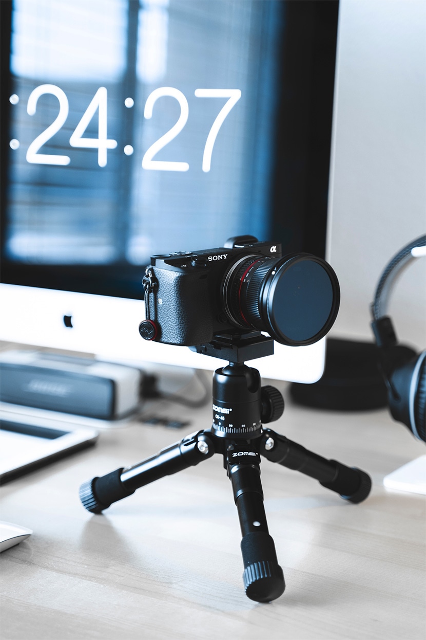 Sony camera mounted on a tripod in front of a desktop computer with large digital clock display.