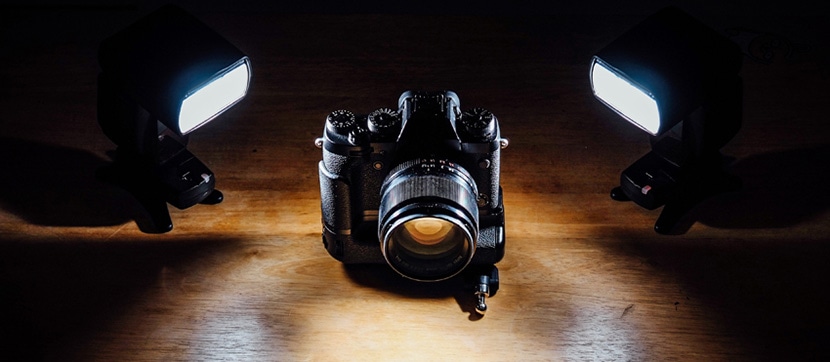 Vintage camera positioned between two flash units on a wooden surface, illuminated dramatically from both sides.