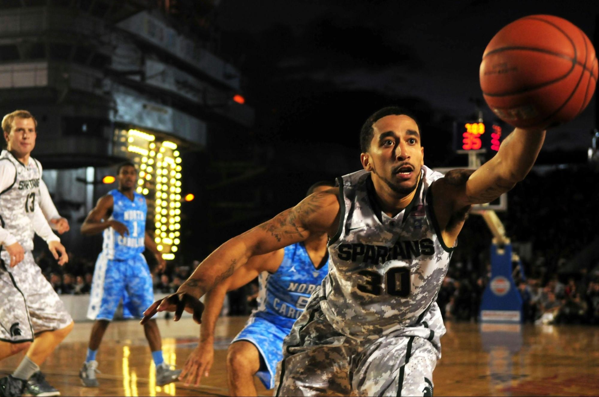 Two basketball players competing for the ball in an indoor court, with expressions of intense focus and energy.