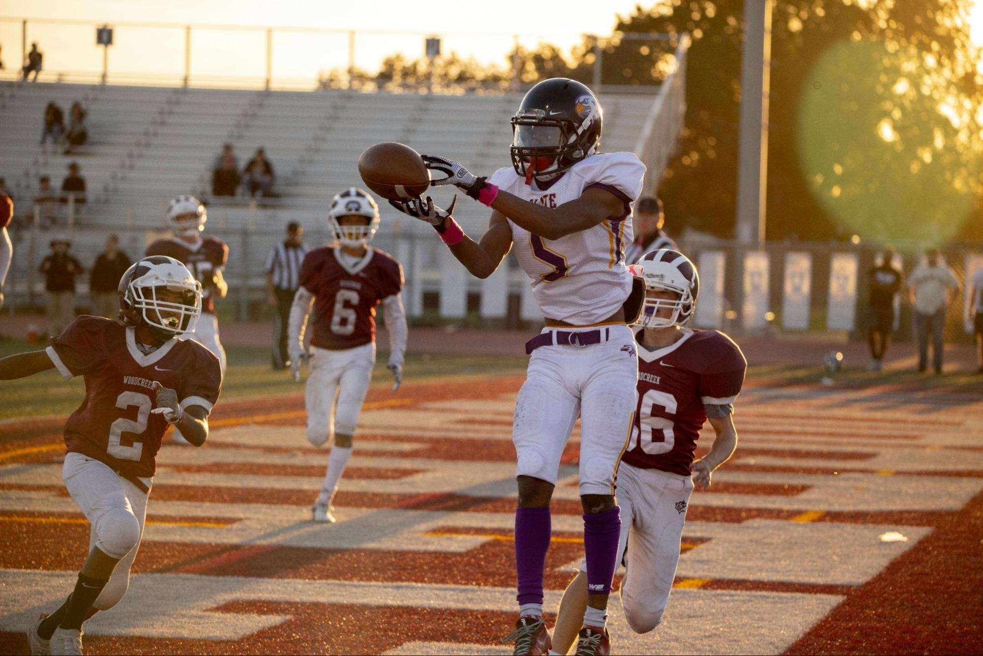 Young football players jumping and celebrating a goal on an outdoor field during sunset.